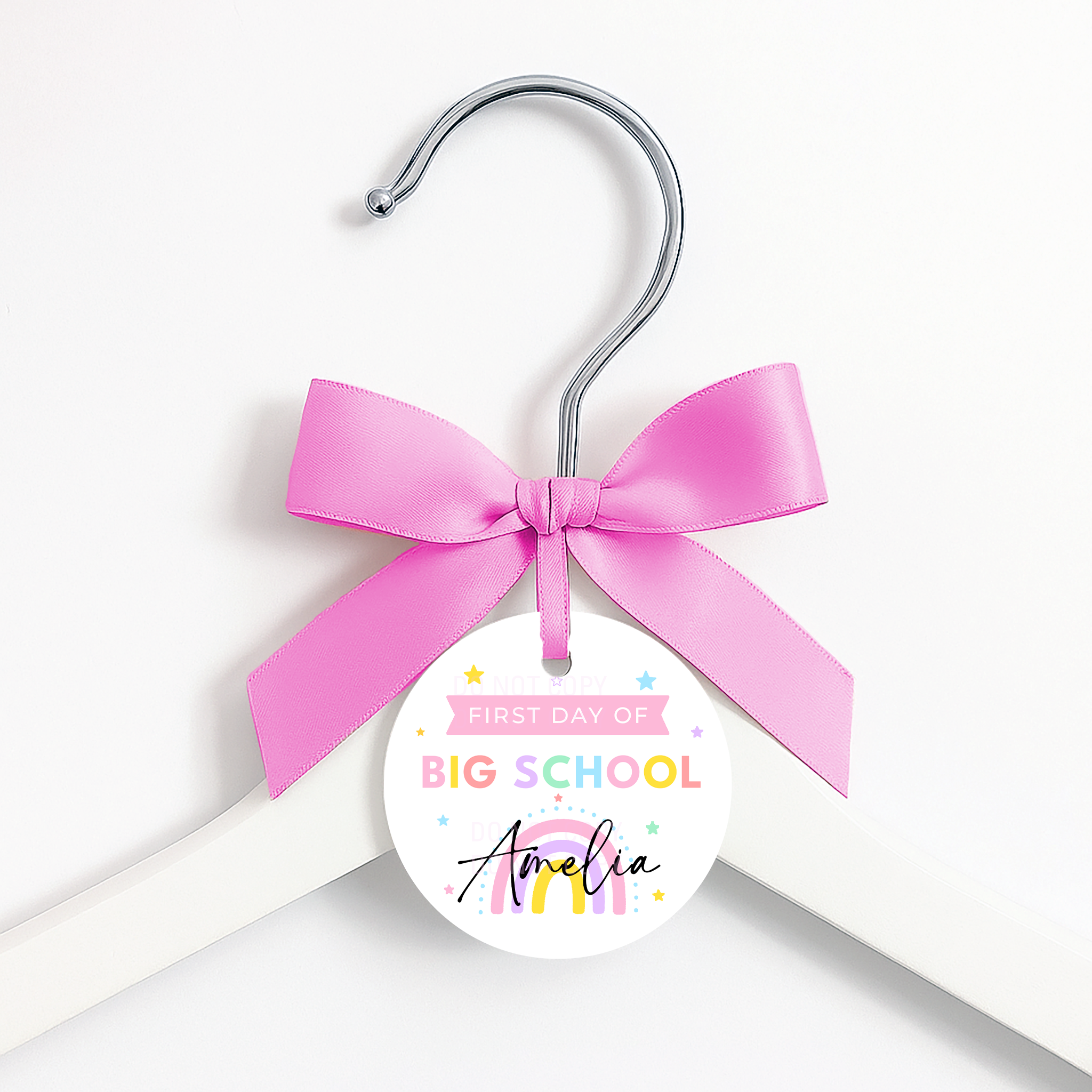 A white wooden hanger with a silver metal hook, decorated with a bright pink satin bow and a round white tag that reads 'FIRST DAY OF BIG SCHOOL in pastel colors.